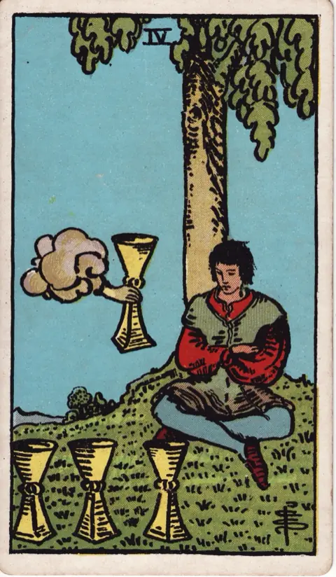 Four of Cups, from the 1909 Rider-Waite-Smith deck: a young man sits with crossed arms under a tree, looking at three cups on the grass, while a hand from a cloud offers him a fourth.