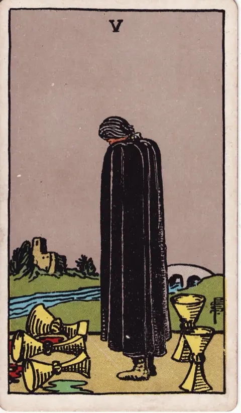 Five of Cups, from the 1909 Rider-Waite-Smith deck: a figure in a black cloak bows his head over three spilled cups, two full cups standing behind him and a bridge leading to a house across the river.