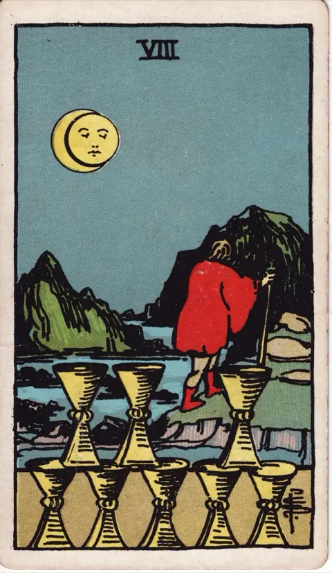 Eight of Cups, from the 1909 Rider-Waite-Smith deck: a man with a walking staff turns away from eight stacked cups and heads into rocky hills under a moon with a face.
