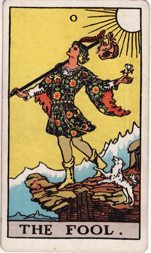 The Fool, from the 1909 Rider-Waite-Smith deck: a young man in a flowered tunic steps toward a cliff edge, a white rose in one hand and a small bundle on a staff over his shoulder, a white dog leaping at his heels and the sun behind him.