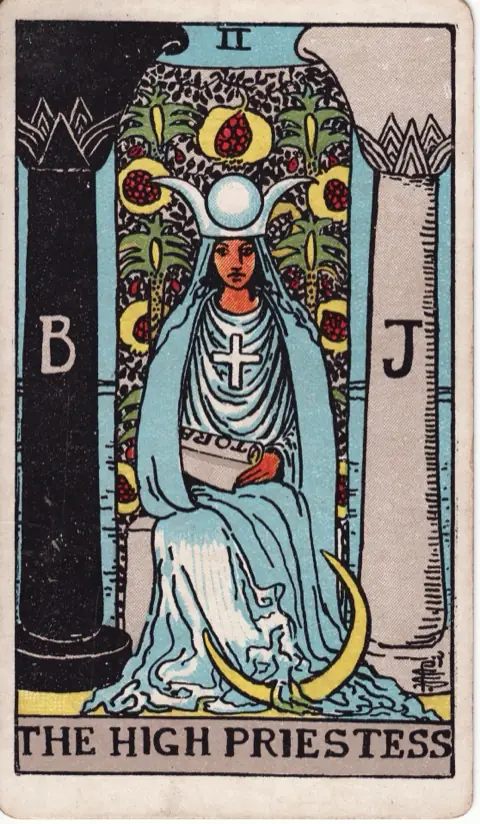 The High Priestess, from the 1909 Rider-Waite-Smith deck: a priestess in blue robes sits between a black pillar marked B and a white pillar marked J, a scroll marked TORA in her lap, a crescent moon at her feet and a veil of pomegranates behind her.