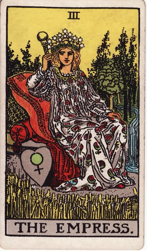 The Empress, from the 1909 Rider-Waite-Smith deck: a woman crowned with twelve stars rests on cushions in a field of ripening wheat, a heart-shaped shield with the sign of Venus beside her and a forest and waterfall behind.