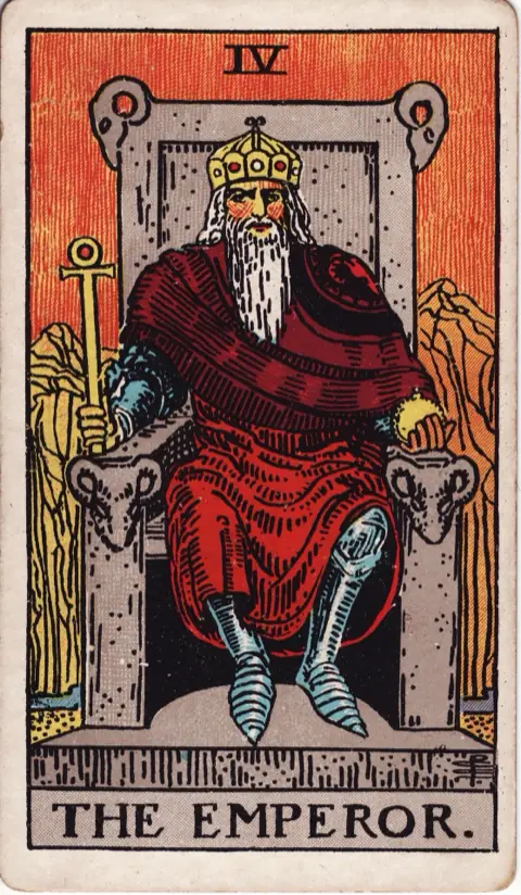 The Emperor, from the 1909 Rider-Waite-Smith deck: a bearded emperor in armour and a red robe sits on a stone throne carved with rams’ heads, holding an ankh sceptre and an orb, bare orange mountains behind him.