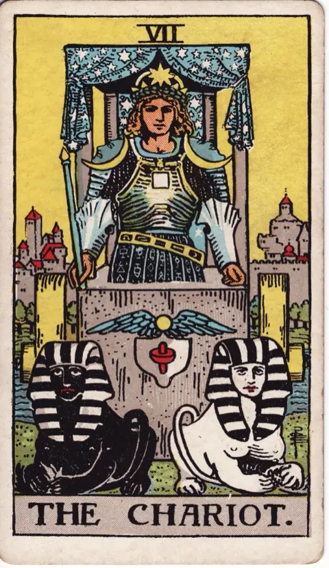 The Chariot, from the 1909 Rider-Waite-Smith deck: a crowned charioteer in armour stands in a chariot under a canopy of stars, a walled city behind him, with a black sphinx and a white sphinx resting in front.