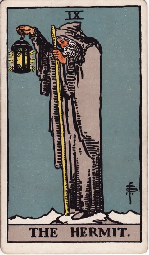 The Hermit, from the 1909 Rider-Waite-Smith deck: an old man in a grey hooded cloak stands alone on a snowy peak, holding up a lantern with a six-pointed star inside it and leaning on a tall staff.