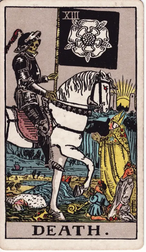 Death, from the 1909 Rider-Waite-Smith deck: a skeleton in black armour rides a white horse and carries a black banner with a white rose, a king fallen beneath it, a bishop pleading, a maiden and a child kneeling, the sun rising between two towers.