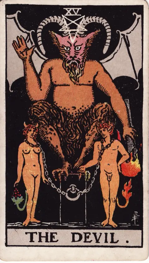The Devil, from the 1909 Rider-Waite-Smith deck: a horned, bat-winged devil crouches on a black pedestal holding a torch pointed down, a naked man and woman with small horns and tails chained loosely to the block below.
