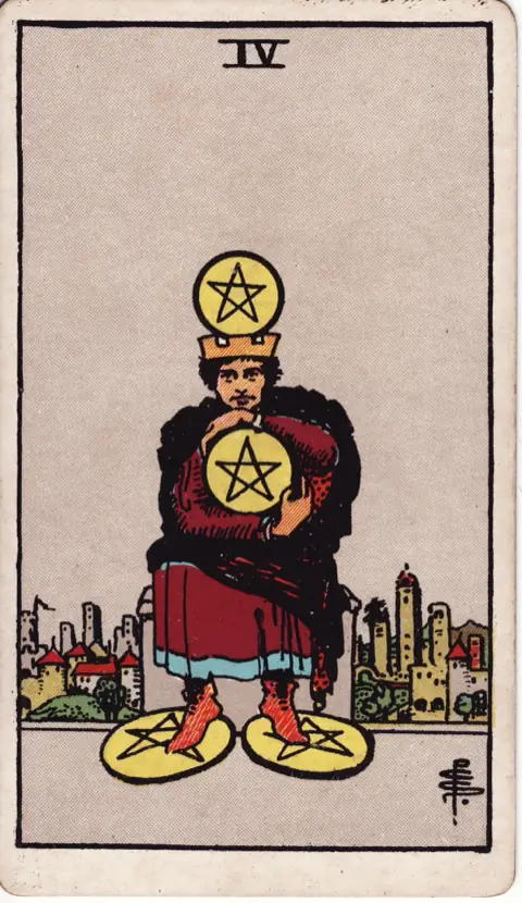 Four of Pentacles, from the 1909 Rider-Waite-Smith deck: a crowned man sits on a stone seat clutching a pentacle to his chest, one under each foot and one on his crown, a city behind him.