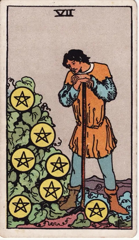Seven of Pentacles, from the 1909 Rider-Waite-Smith deck: a young farmer leans on his hoe and looks at seven pentacles growing on a green bush.