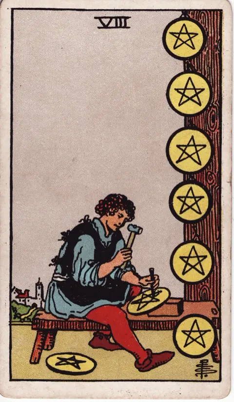 Eight of Pentacles, from the 1909 Rider-Waite-Smith deck: a craftsman sits at a bench carving a pentacle, six finished ones hanging on a post beside him and one at his feet, a town in the distance.