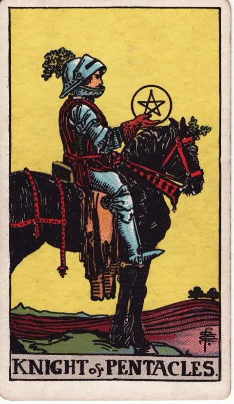 Knight of Pentacles, from the 1909 Rider-Waite-Smith deck: a knight in armour sits still on a heavy black horse in a ploughed field, holding a pentacle and looking at it.