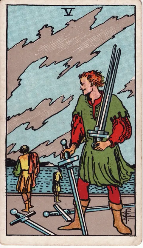 Five of Swords, from the 1909 Rider-Waite-Smith deck: a smirking man gathers up three swords while two beaten figures walk away toward the sea, two more swords lying on the ground under a torn sky.