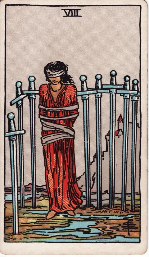 Eight of Swords, from the 1909 Rider-Waite-Smith deck: a woman in a red dress stands bound and blindfolded among eight swords stuck in the mud, a castle on a cliff behind her.