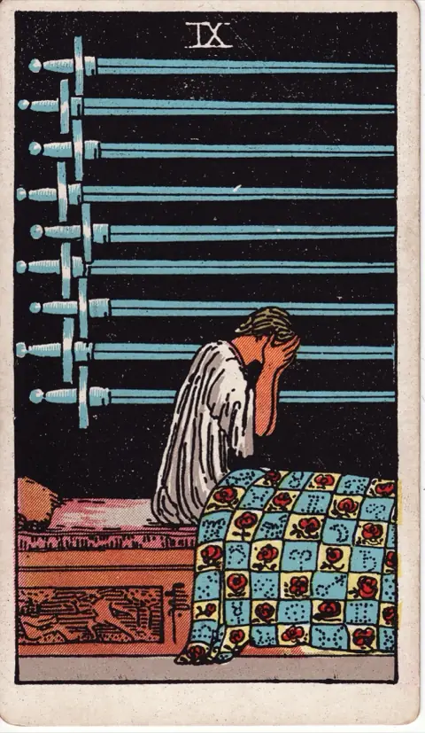 Nine of Swords, from the 1909 Rider-Waite-Smith deck: a woman sits up in bed with her face in her hands, nine swords hanging across the dark wall behind her.
