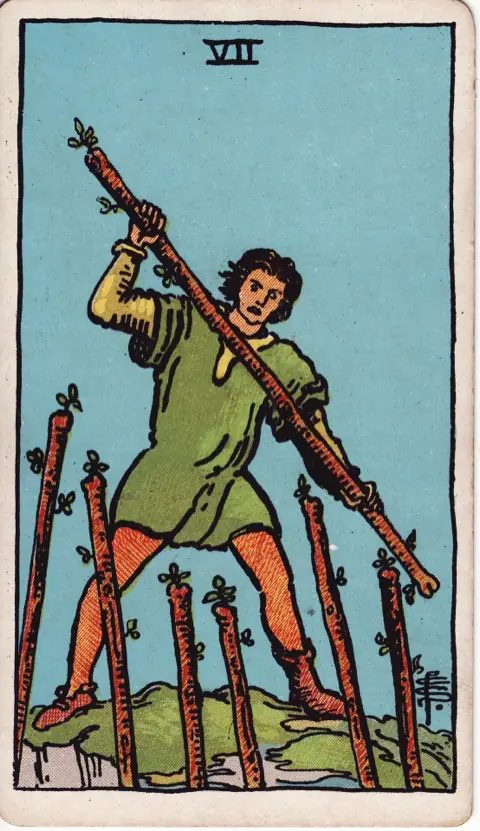 Seven of Wands, from the 1909 Rider-Waite-Smith deck: a young man on high ground holds a wand across his body, holding off six wands rising toward him from below.